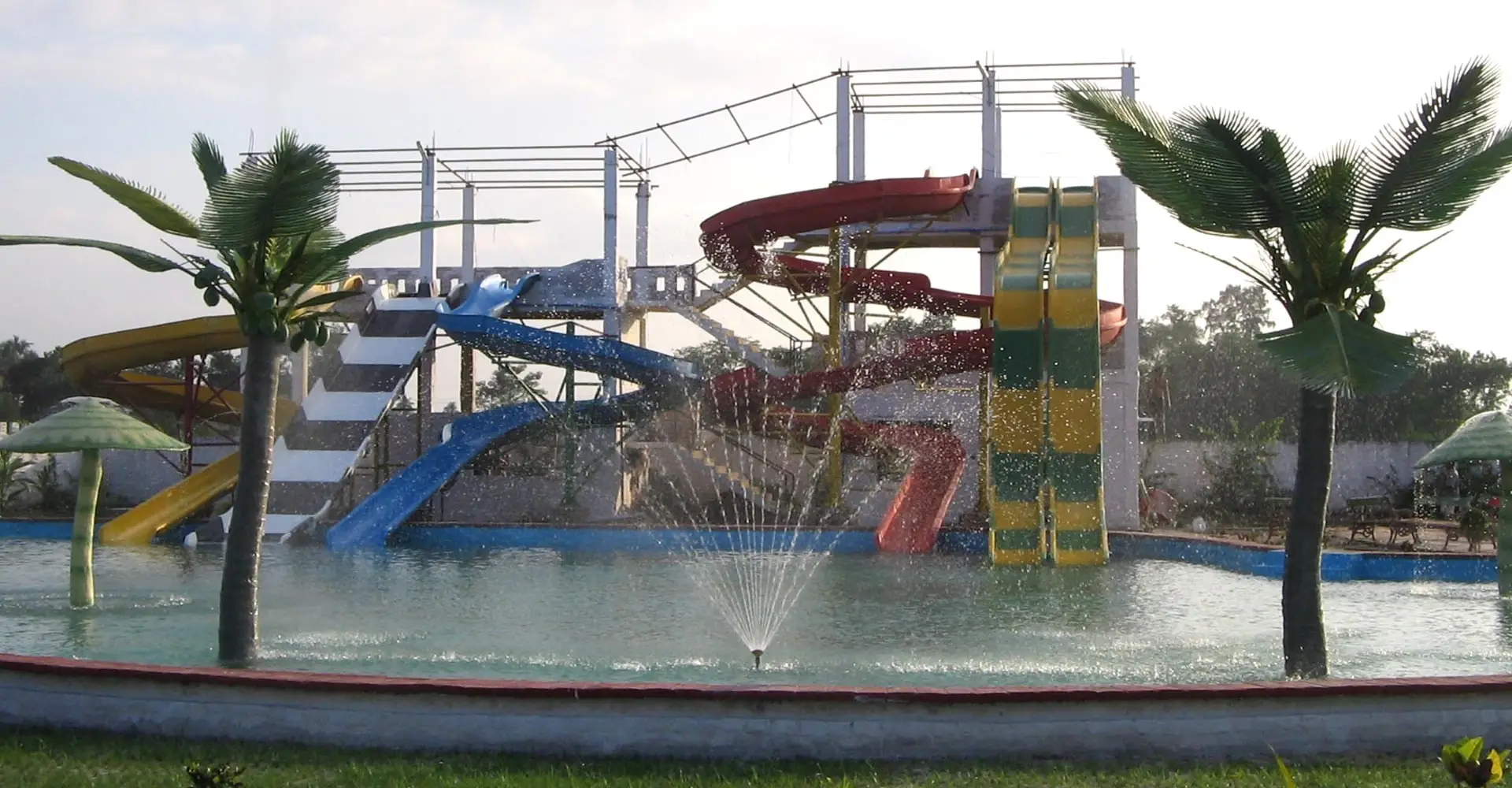 Water park with colourful slides, a fountain and palm trees around a pool
